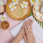 Young woman applying natural scrub on hands against white background. Spa treatment and product for female hand spa, massage, perfumed flowers water and candles, Relaxation. Flat lay. top view.